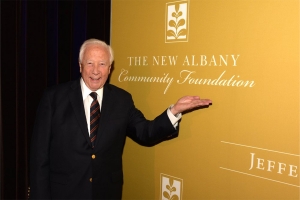 man standing if front of a large yellow sign with the New Albany Community Foundation logo on it.