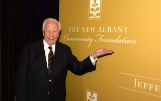 man standing if front of a large yellow sign with the New Albany Community Foundation logo on it.