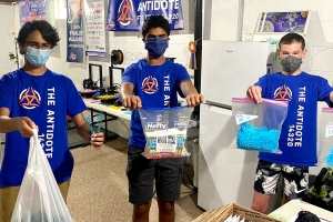 3 younger boys wearing face masks and holding up plastic bags of COVID-19 supplies.