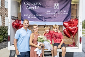 Angela Douglas holding flowers and posing behind an open cargo truck full of boxes with her husband and two sons.