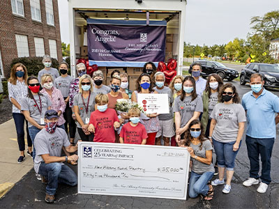 A group of people posing behind an open cargo truck full of boxes. Group members are wearing face masks and holding a $35,000 check in front of them for Angela Douglas.