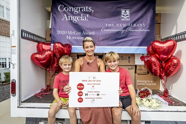 Angela Douglas, winner of the 2020 McCoy Award for community service seated in back of an open food delivery truck with her two young sons.